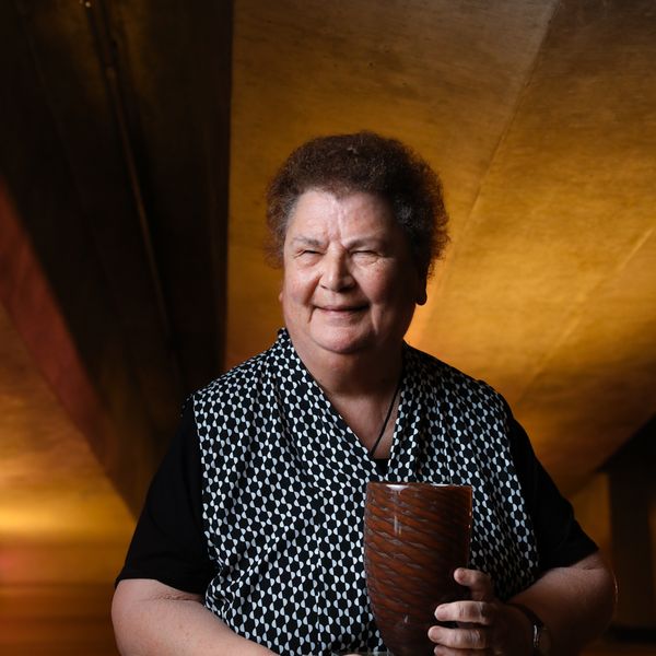 Photo of a senior woman with curly hair with award with designed wooden background at Sydney Opera House.