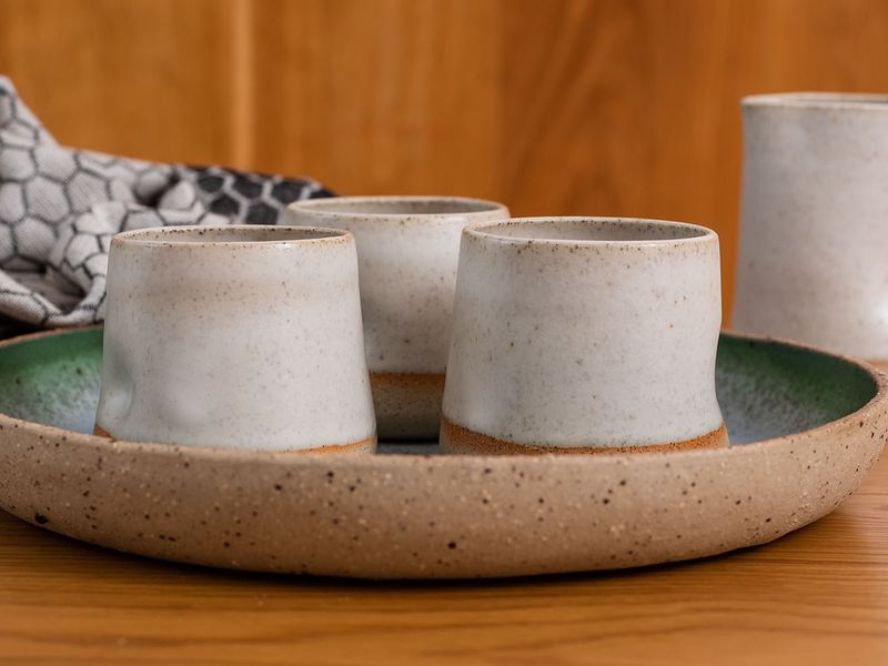 Photo of handmade ceramic mugs in  creamy beige colour on a platter with a wooden background.