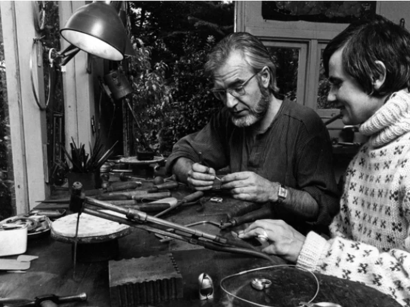 Black and white photo of a man with beard and woman with short hair in a jewellery studio looking closely at a work